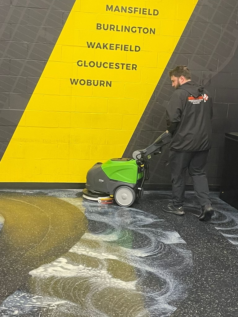 Dustbusters technician running an auto scrubber across a fitness facility floor