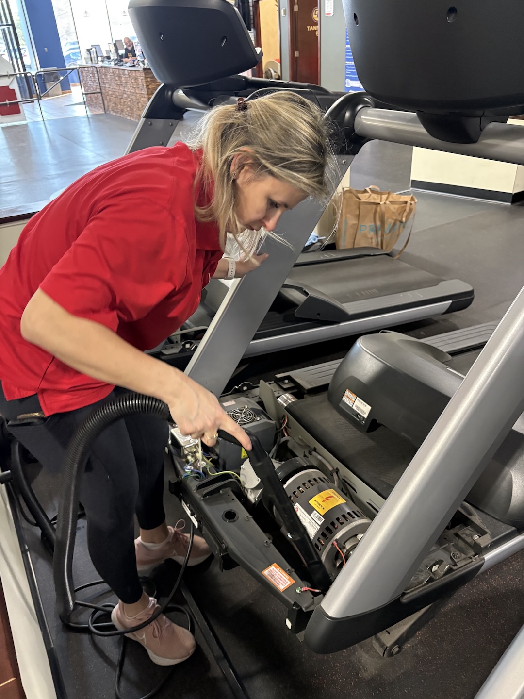 Dustbusters team member vacuuming dust from inside a treadmill at a fitness center
